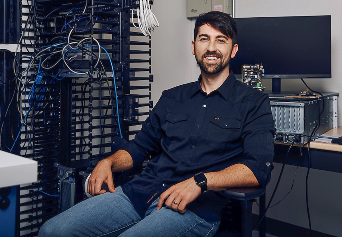 Nick Harris in a black shirt and jeans sits near computer parts.