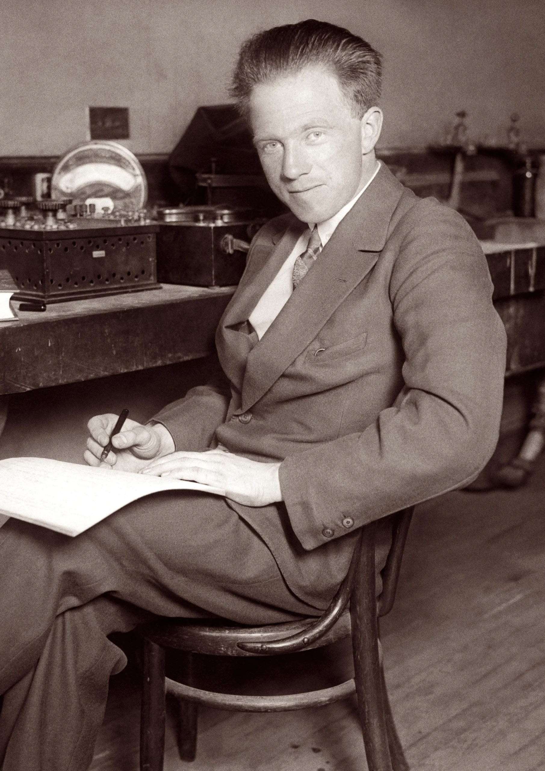 A man sits in a laboratory and scribbles in a notepad.