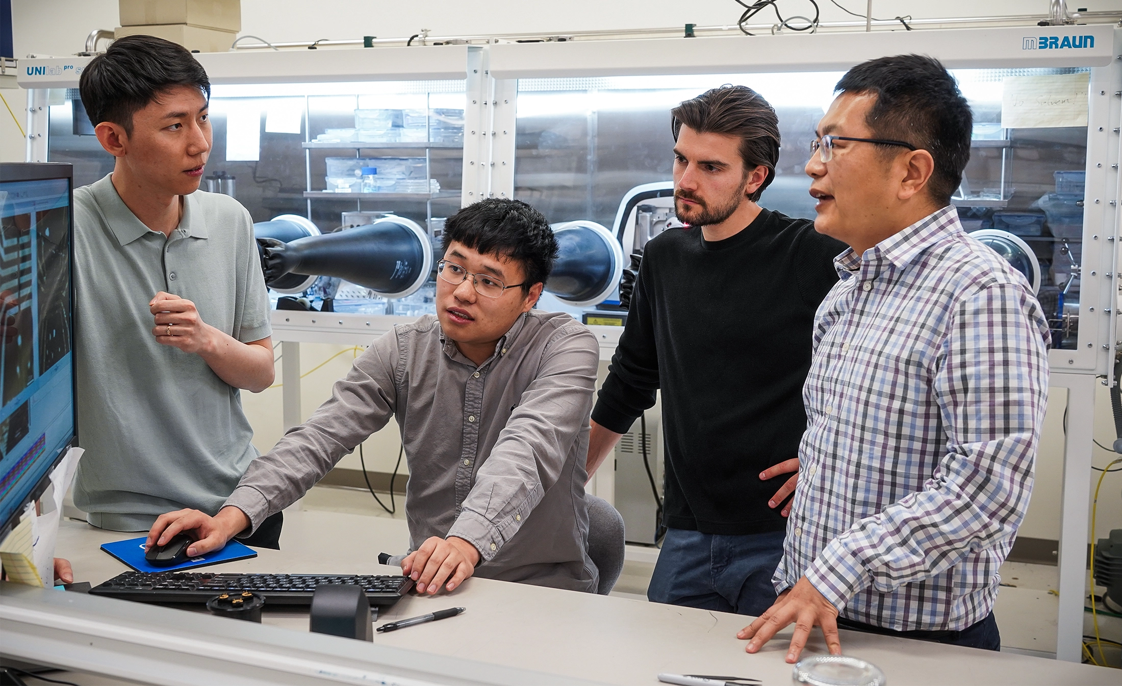 Four men huddle around a computer screen in a lab.