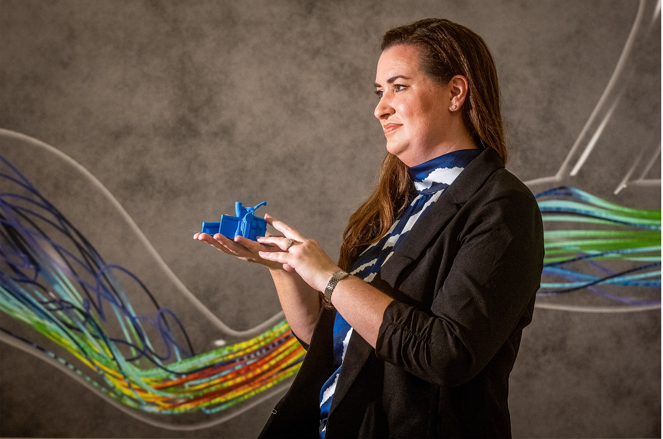 Amanda Randles holds a blue object in front of a gray wall with colorful lines