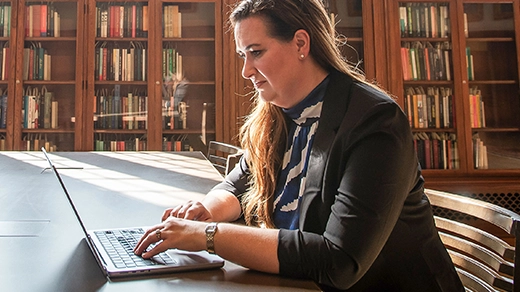 Amanda Randles sits at a desk using a laptop in a library reading room