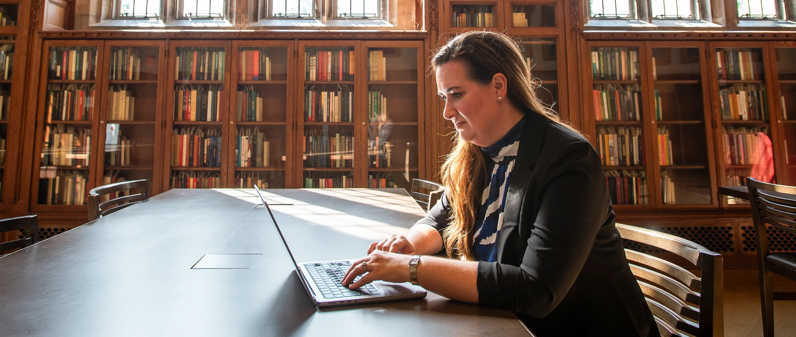 Amanda Randles sits at a desk using a laptop in a library reading room