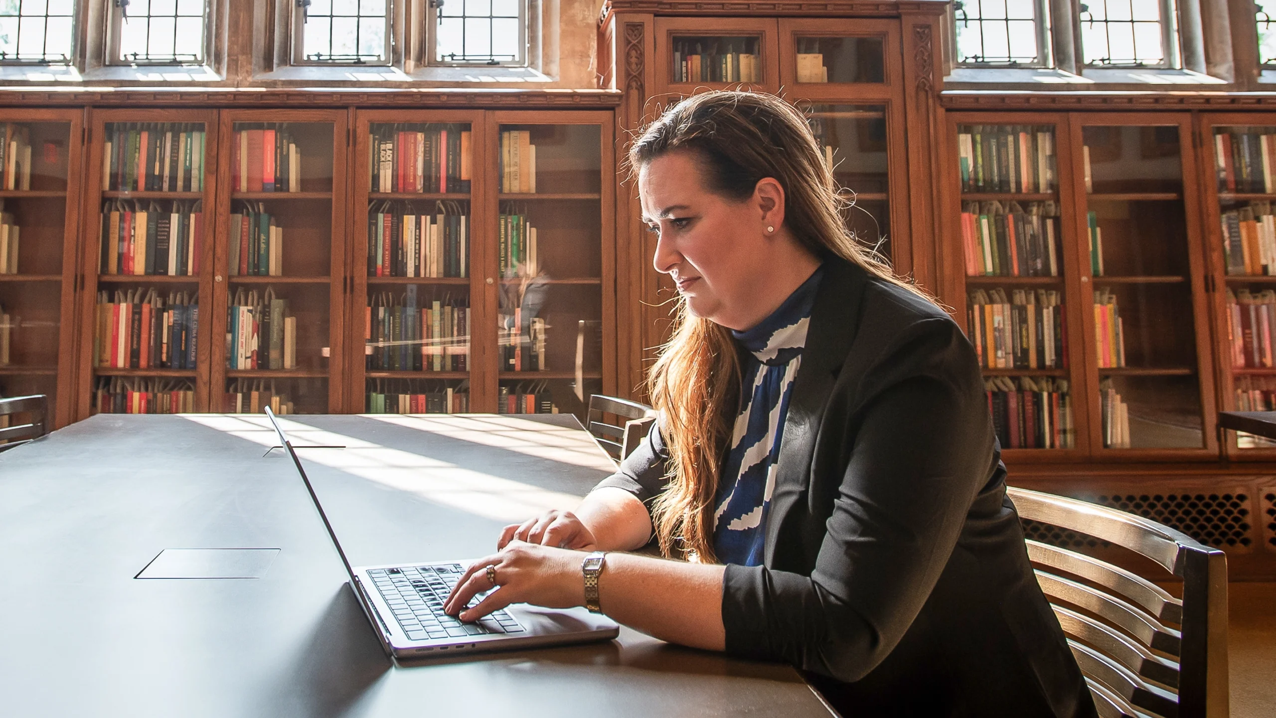 Amanda Randles sits at a desk using a laptop in a library reading room