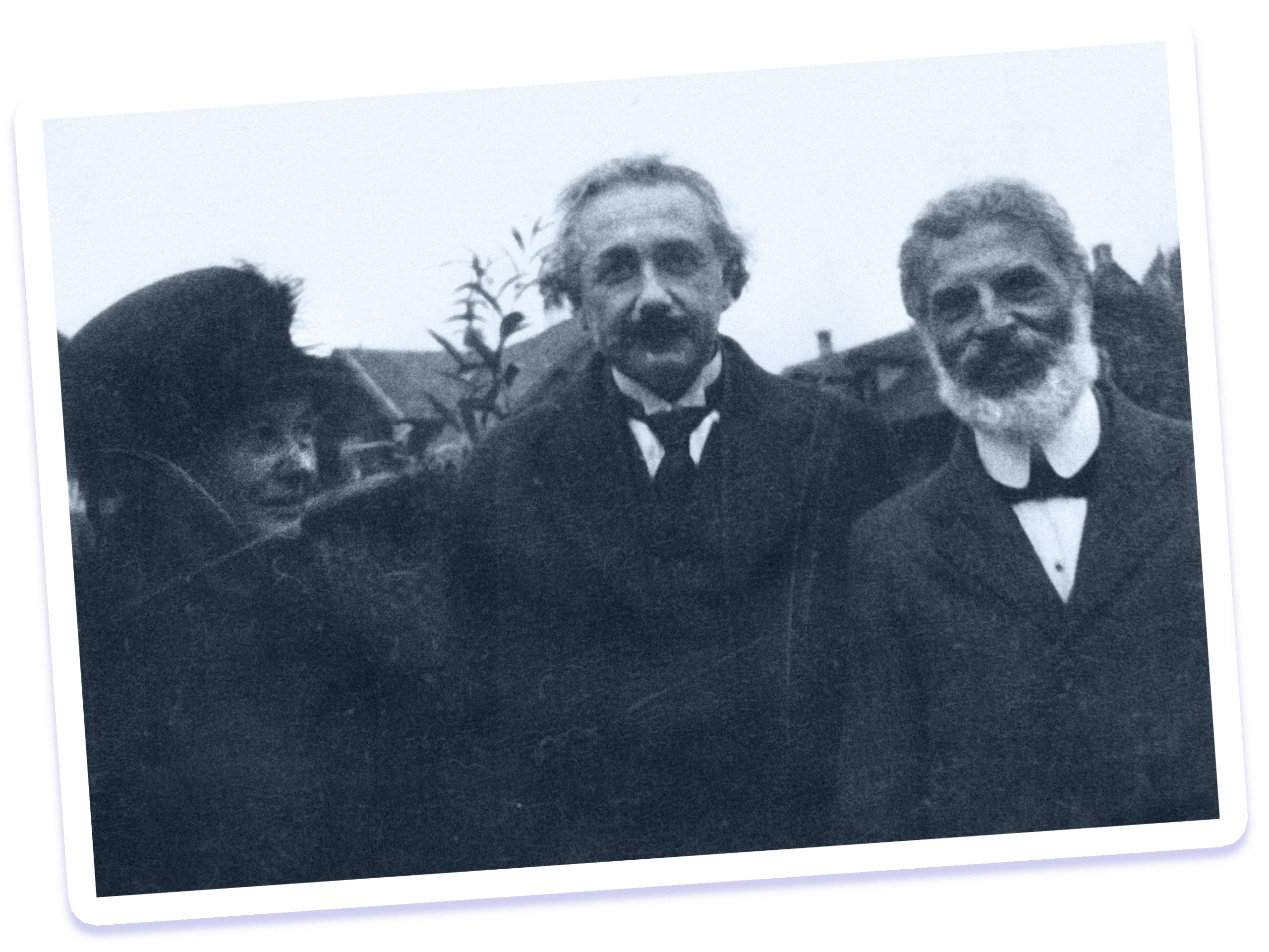 Black-and-white photo of three people standing outside in front of a house, smiling amicably. The man in the middle is Einstein.