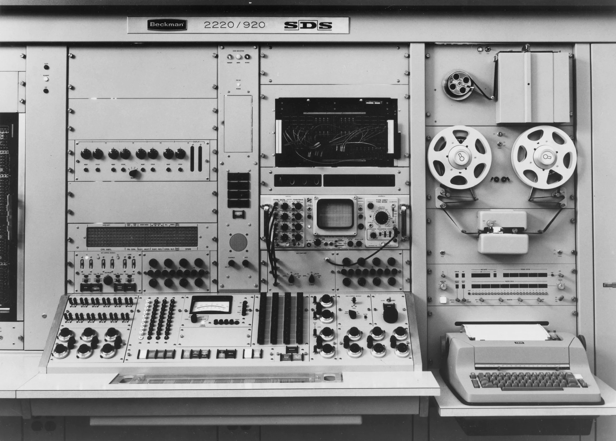 A complicated machine with tape, a typewriter, and multiple switches, dials and screens.