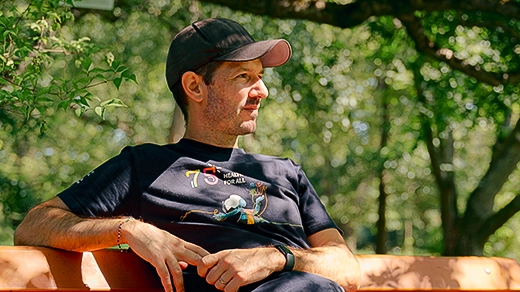 Sébastien Calvignac-Spencer sits on a park bench wearing a T-shirt and baseball cap.