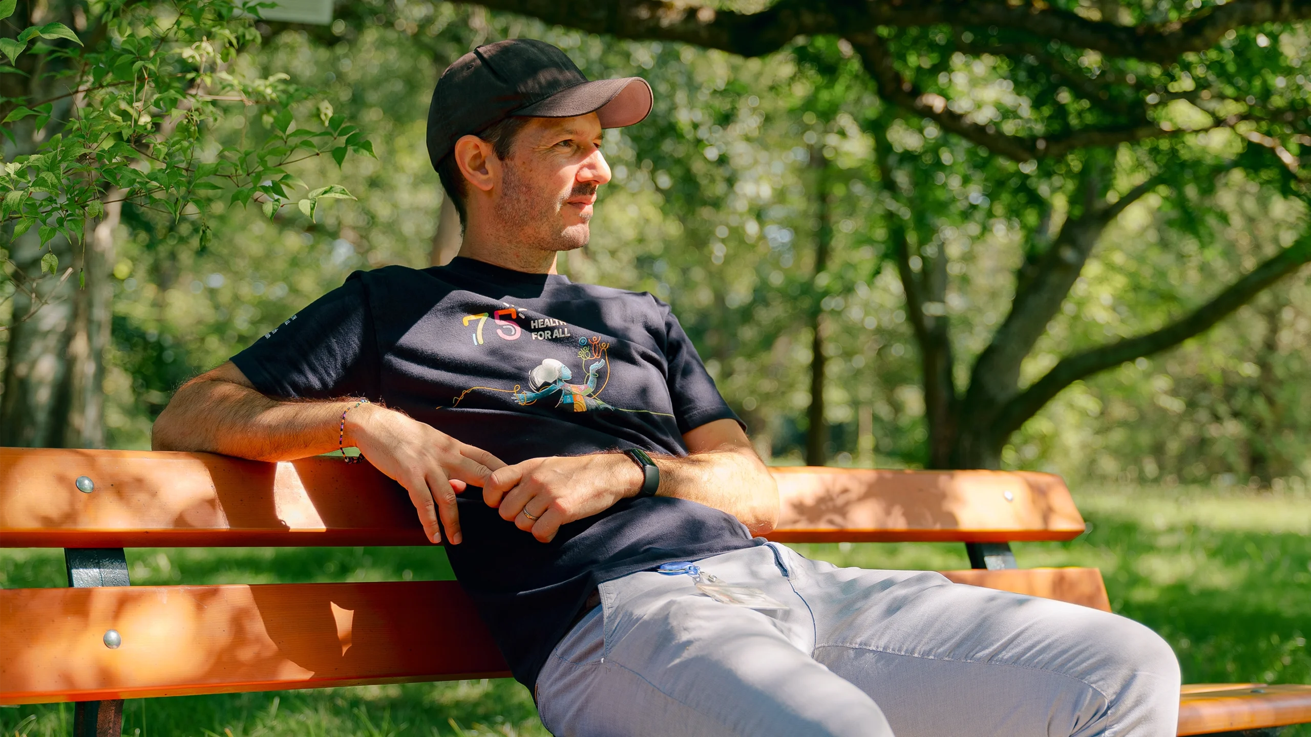 Sébastien Calvignac-Spencer sits on a park bench wearing a T-shirt and baseball cap.