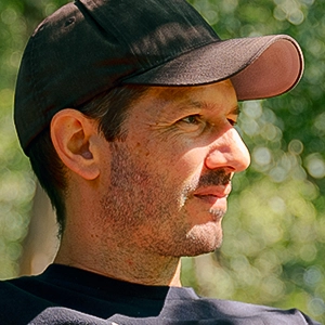 Sébastien Calvignac-Spencer sits on a park bench wearing a T-shirt and baseball cap.