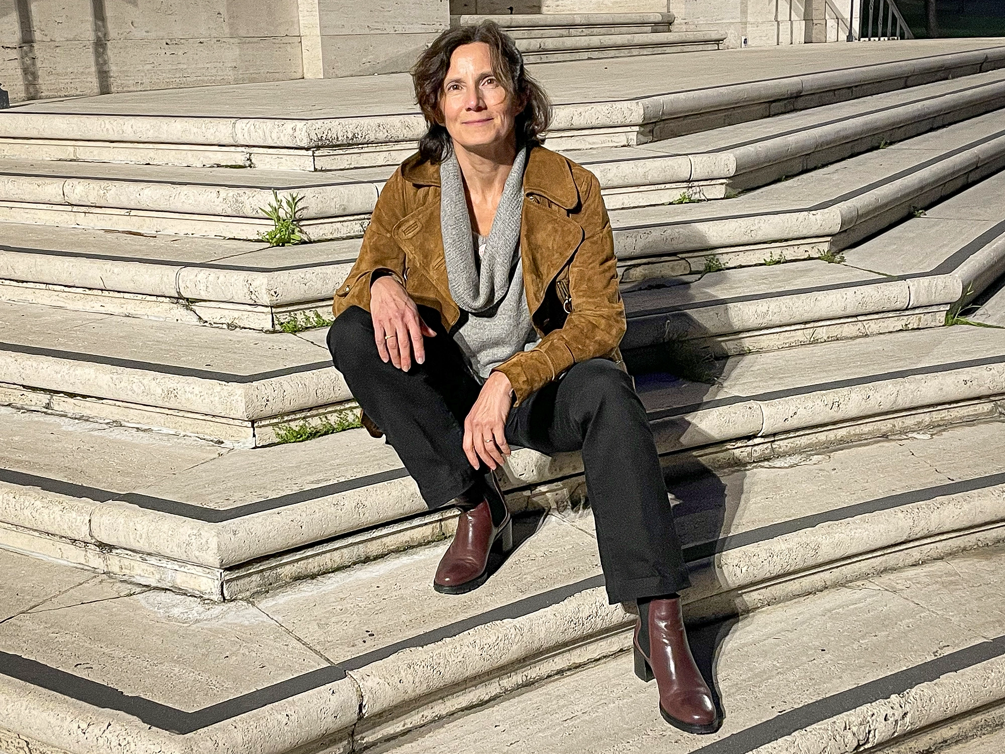 A woman with brown hair sits on some stone steps.