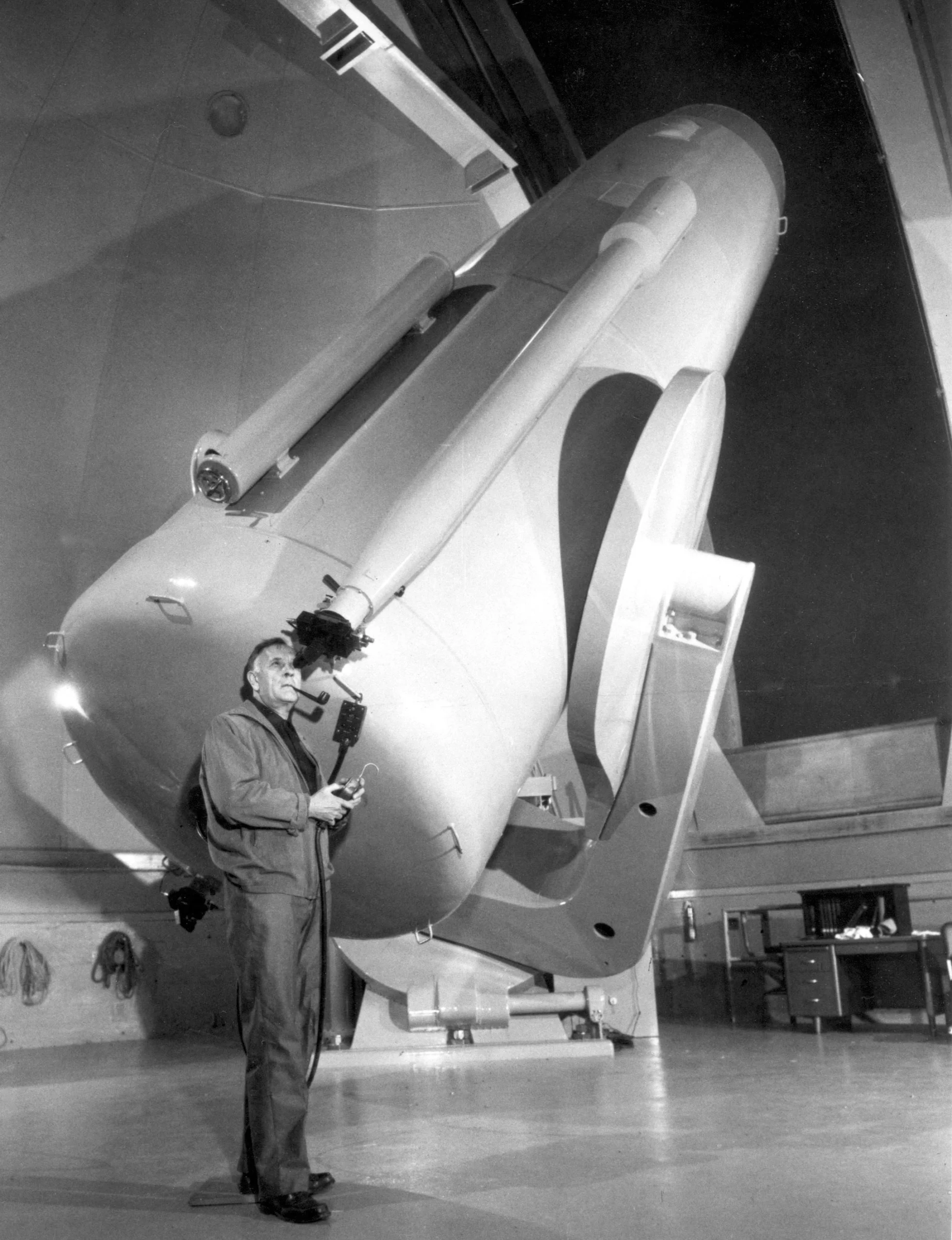 Black-and-white photo of a man with a pipe looking into the eyepiece of a huge telescope.