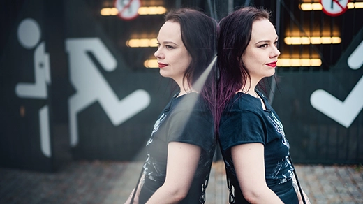 A woman with black hair in a black T-shirt leaning against a mirror and seen in reflection.