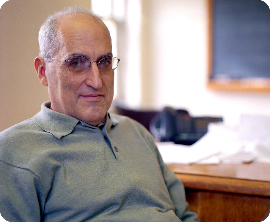 A bespectacled man in a green shirt sits in an office.