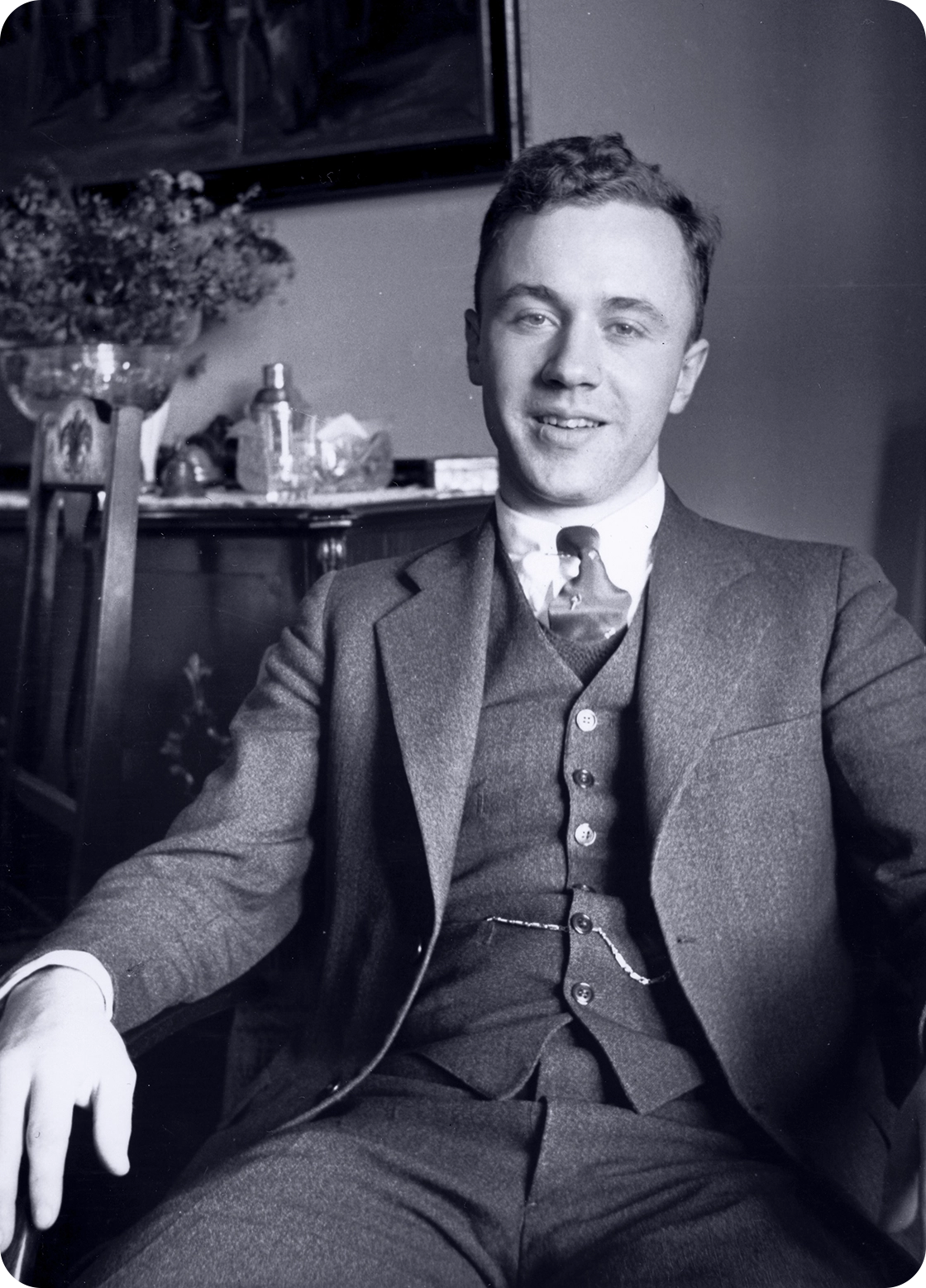 Black and white photo of a smiling young man in a suit sitting in a chair.