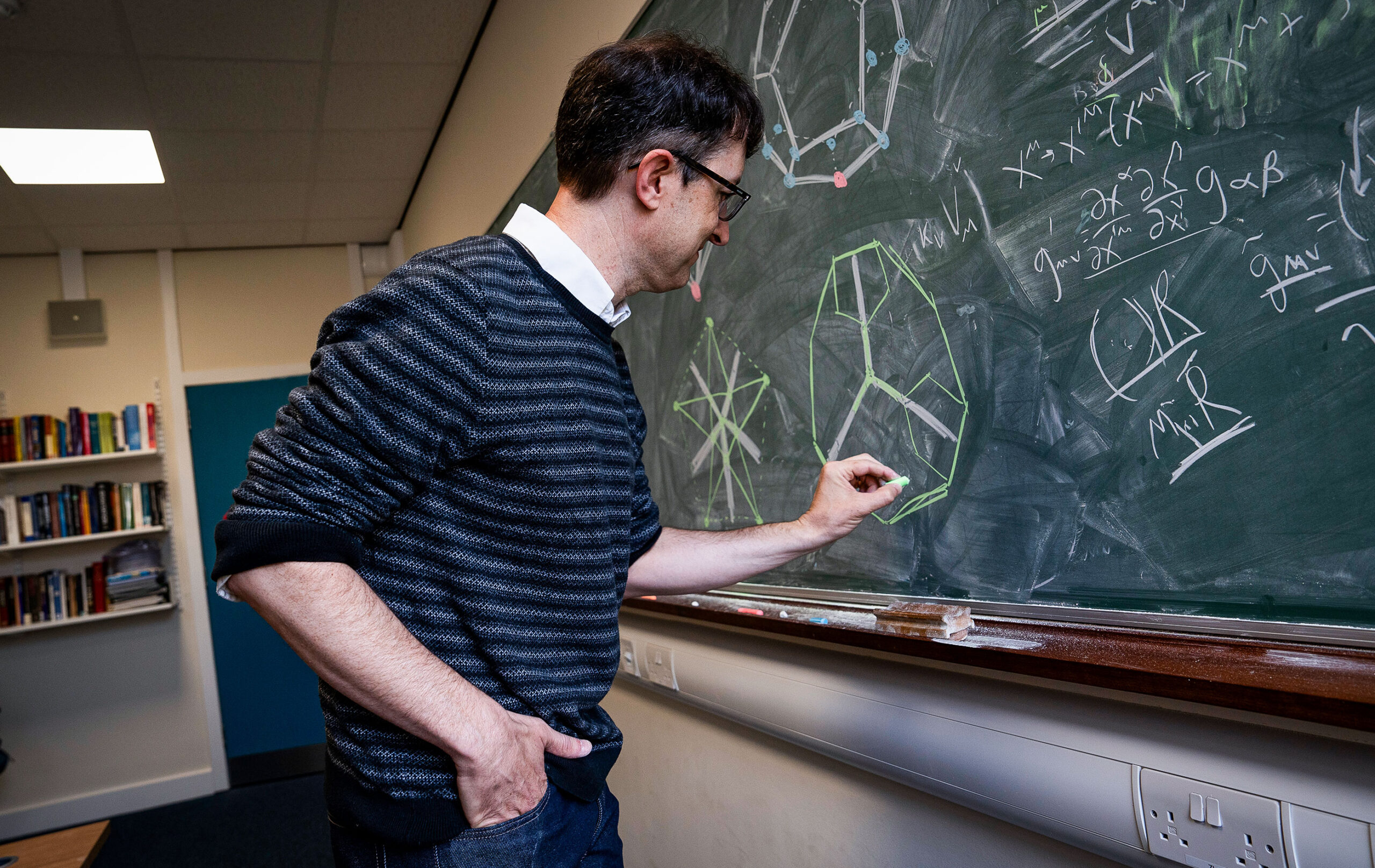 A man draws geometric figures on a blackboard.