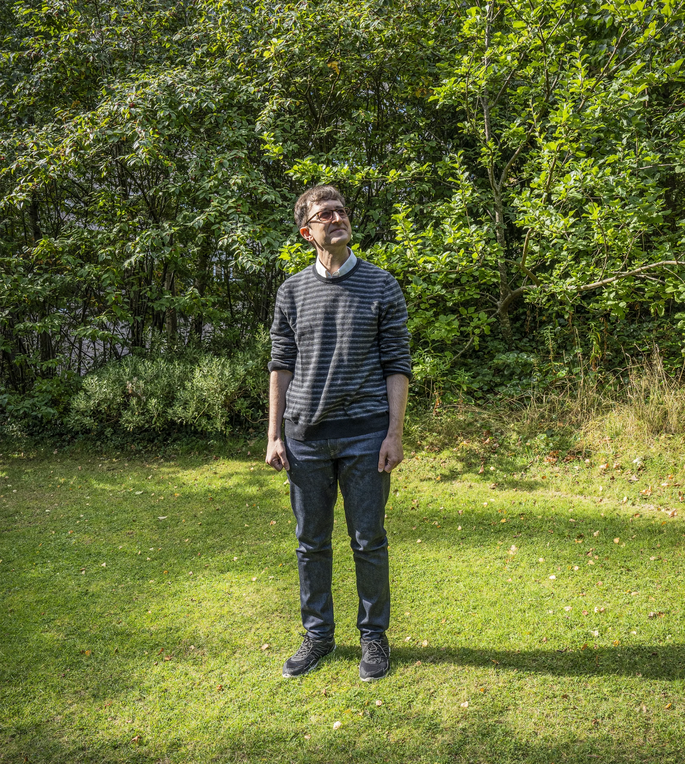 A man stands on some grass in front of trees.