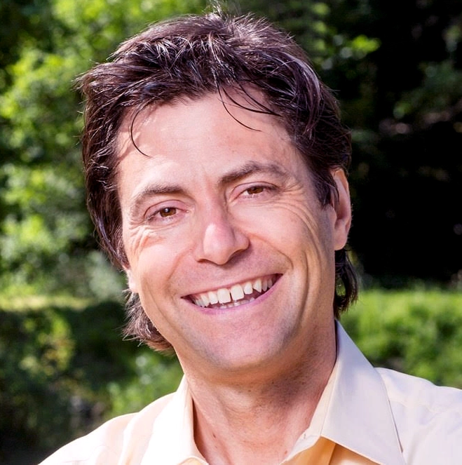 Max Tegmark in a yellow shirt with trees and grass in the background