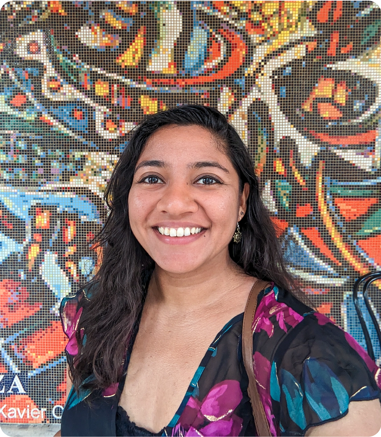 A woman stands in front of a colorful mosaic.