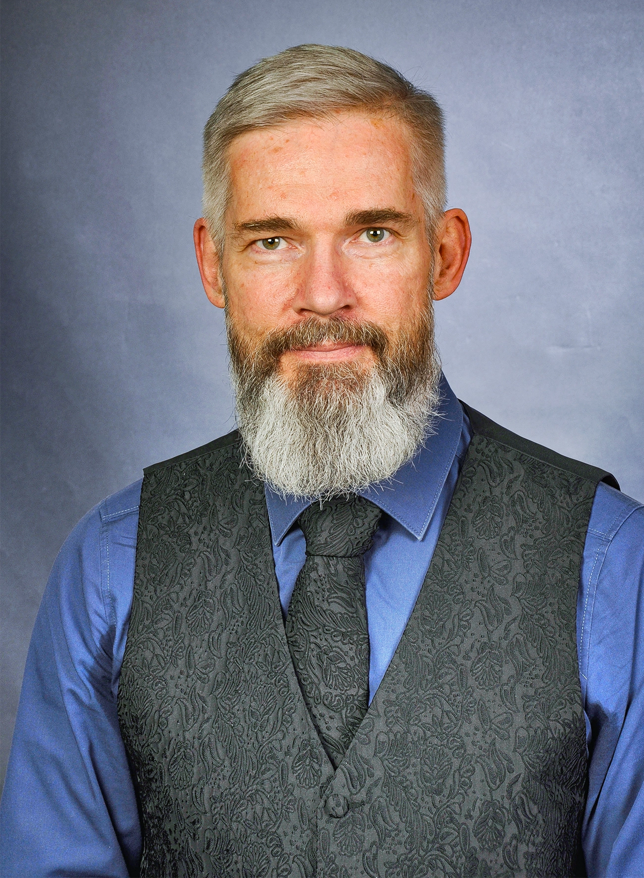 Andreas Nieder has a gray beard and wears a black vest and tie.