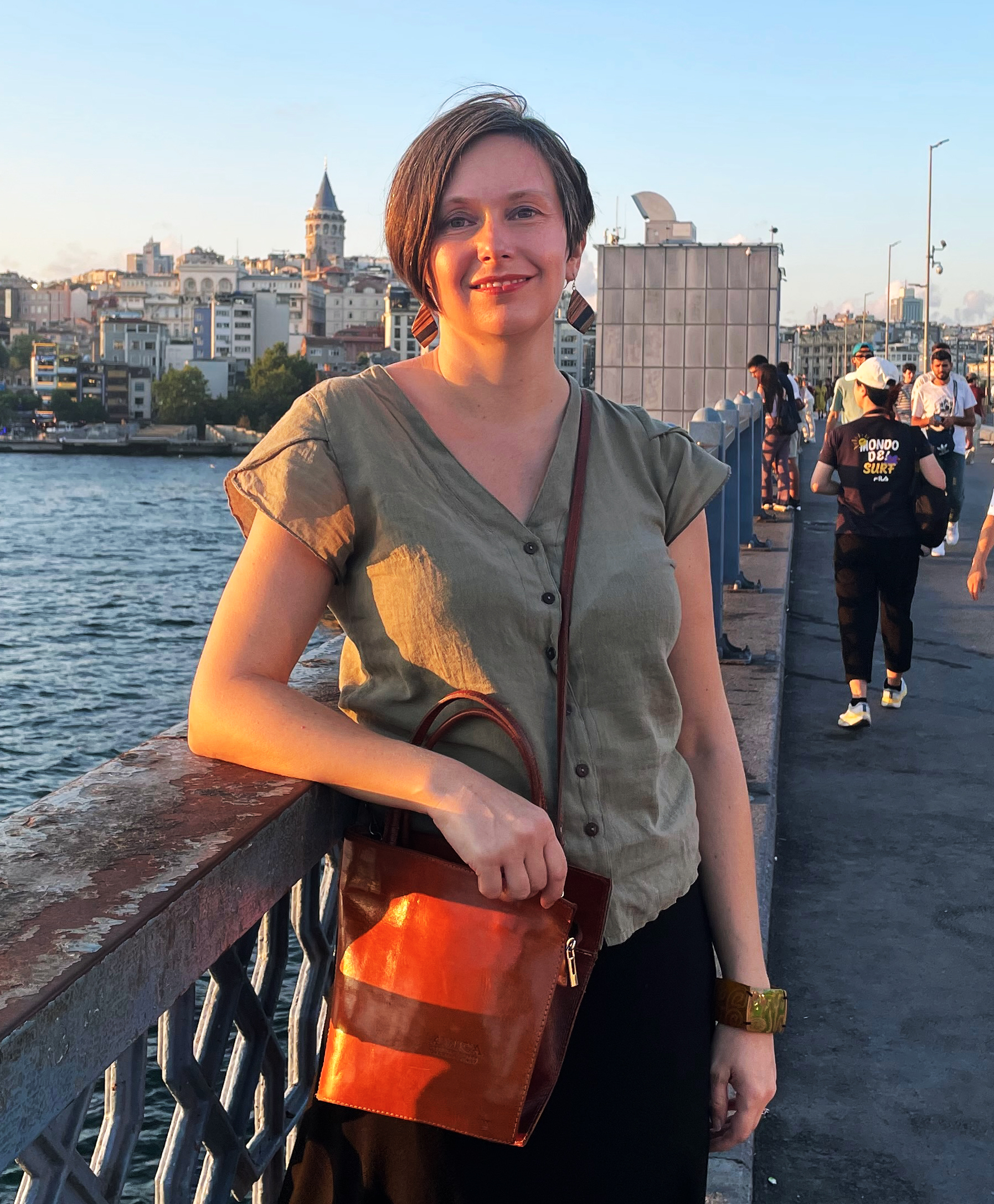 A woman by a bridge with a red bag during sunset