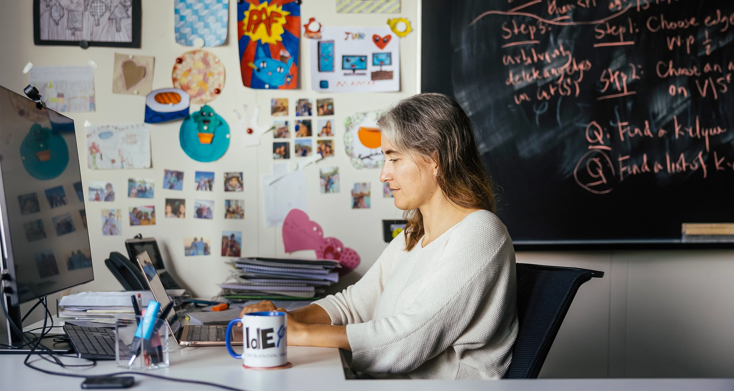 Lenka Zdeborová uses a laptop on a desk with colorful artwork on the wall behind her