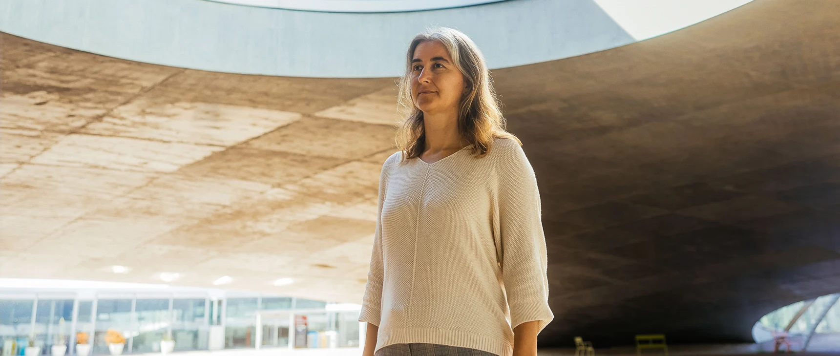 Lenka Zdeborová in a tan sweater stands outside in a large pavilion