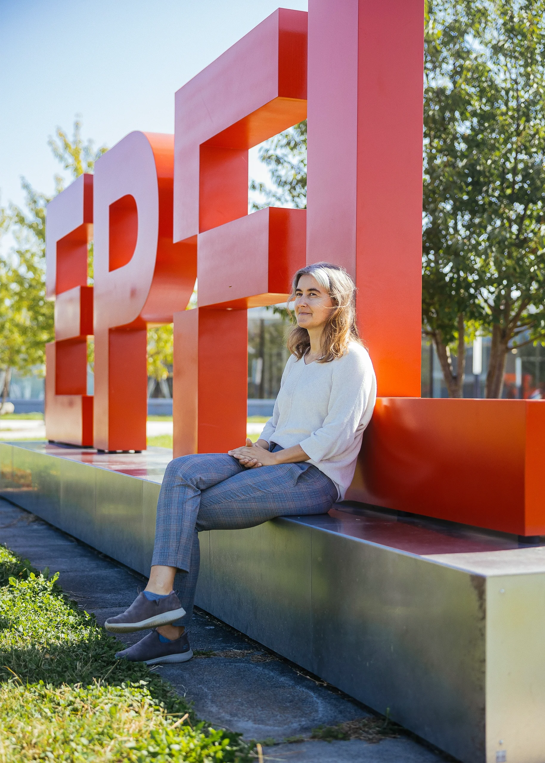 Lenka Zdeborová sits outside on a sculpture of the letters EPFL in red