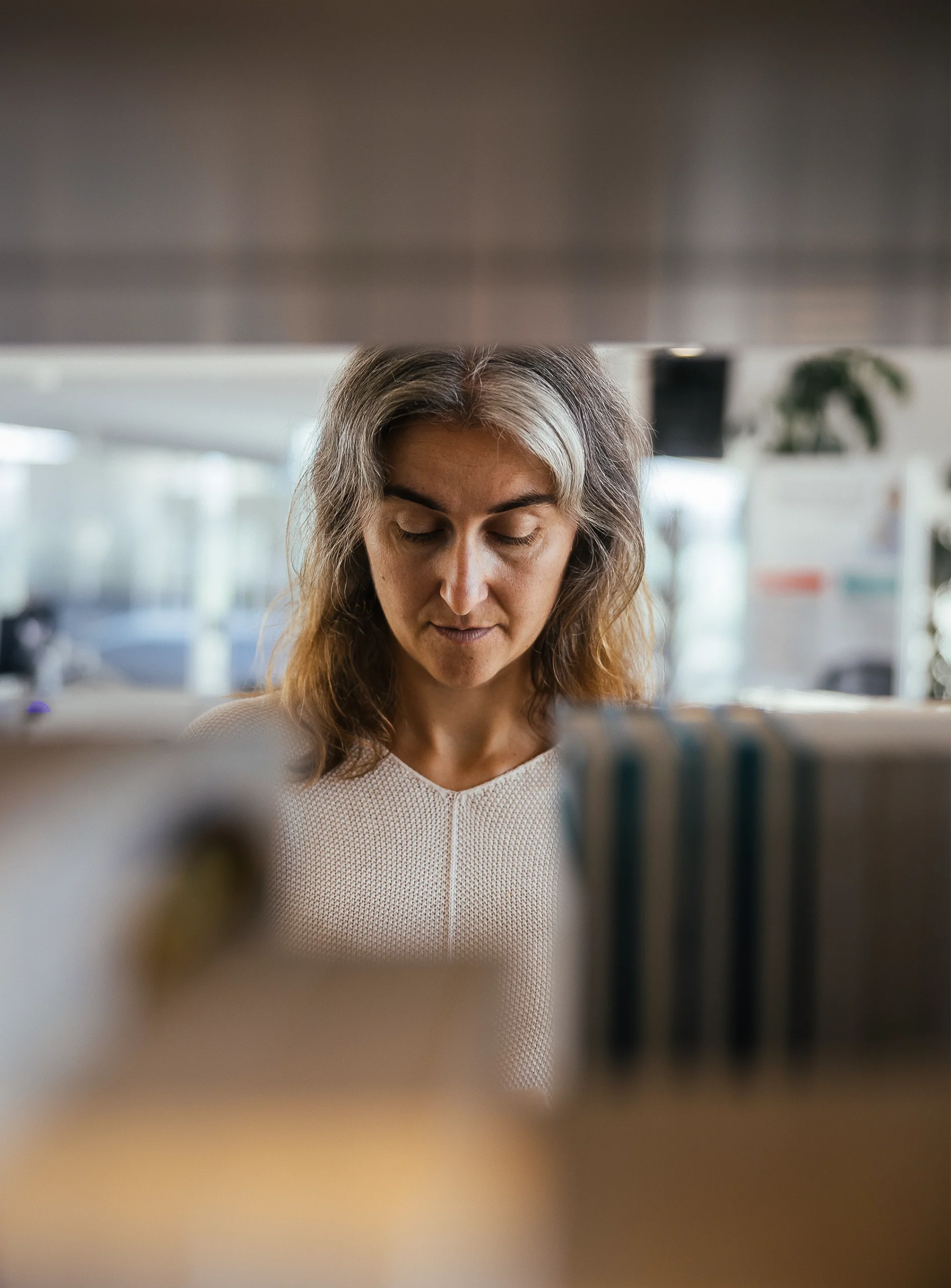 Lenka Zdeborová in a tan sweater looks down, behind an out of focus bookshelf