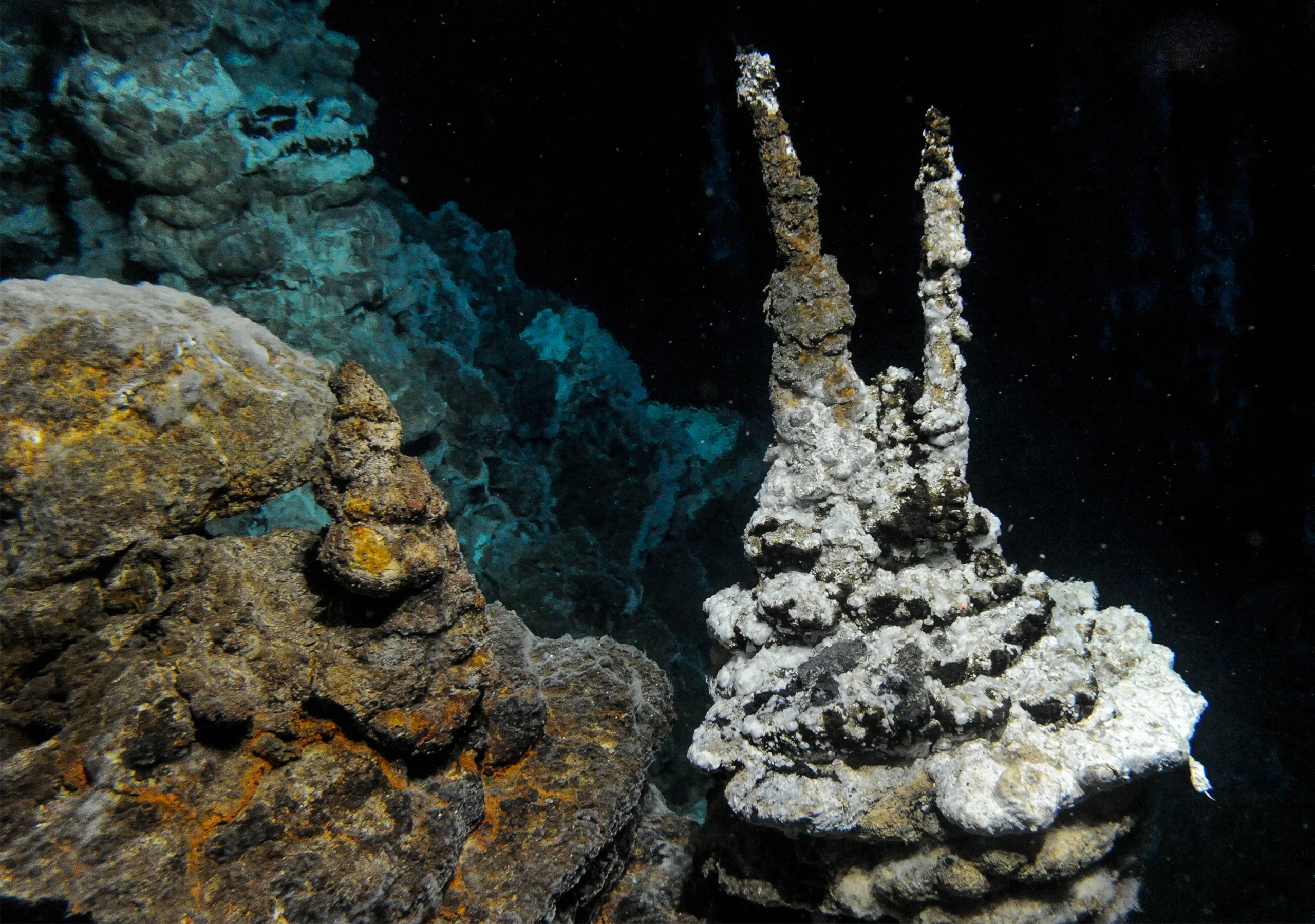 Sulfide deposits accumulate into round, flat mounds and pointed chimneys at this underwater vent.