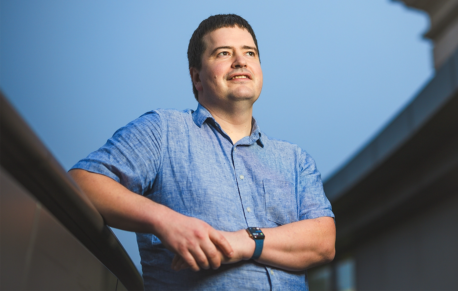 Geoffrey Irving in a blue polo shirt poses outside with the sky and a building behind.