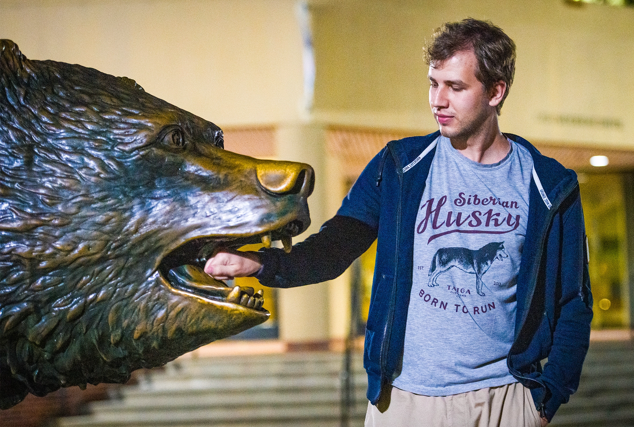 A man stands next to a bear statue with his hand in its mouth