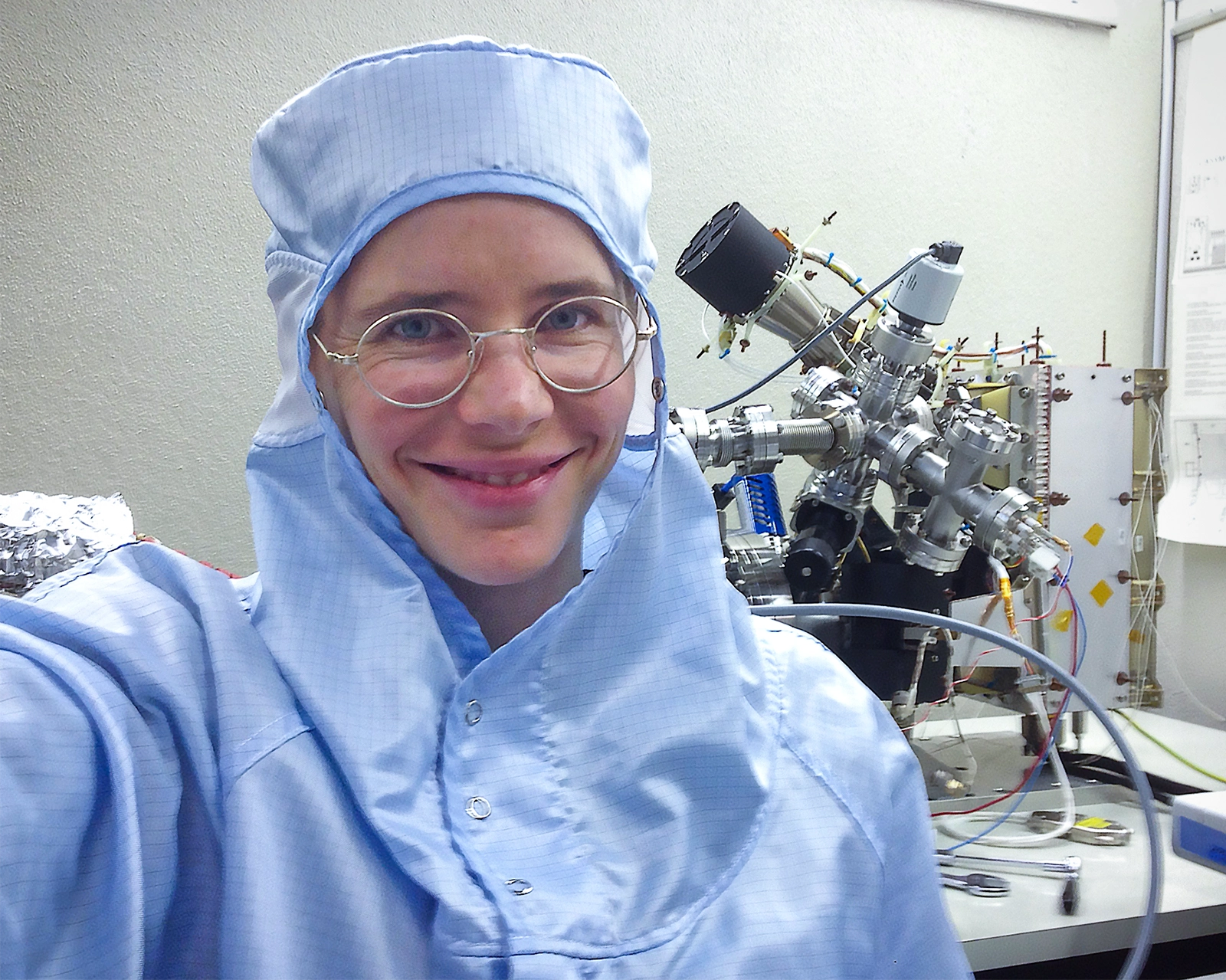 Portrait of a woman in a clean room with scientific equipment behind her.