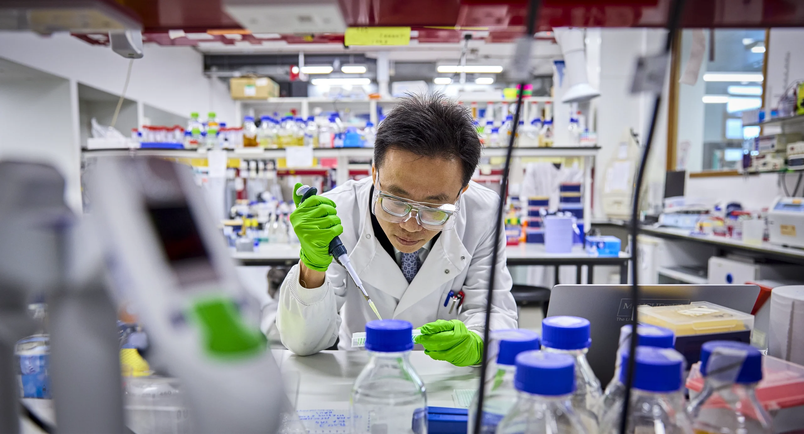 Cai leans over a lab bench while holding a pipette