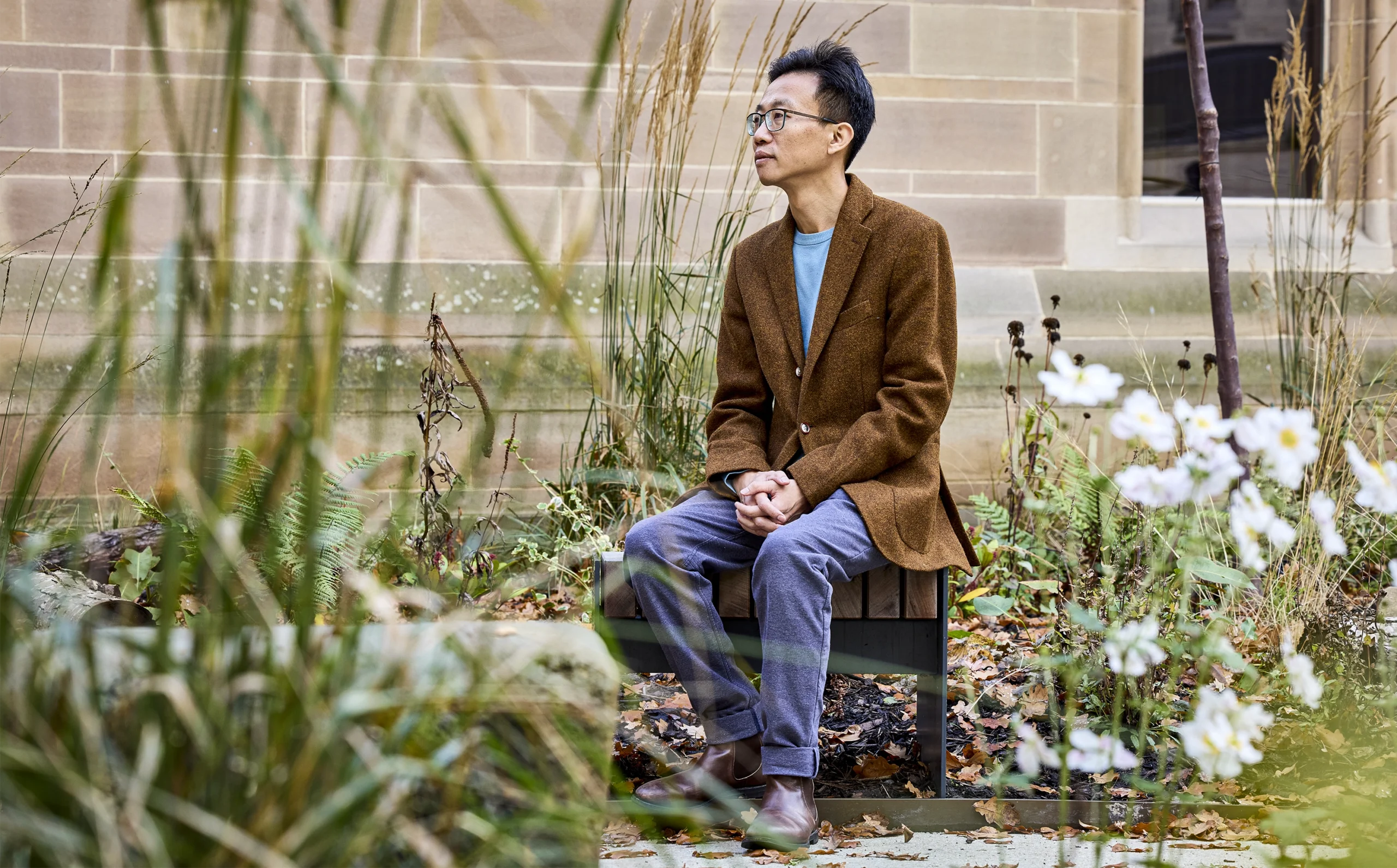 Cai sits on a bench in a flower garden.