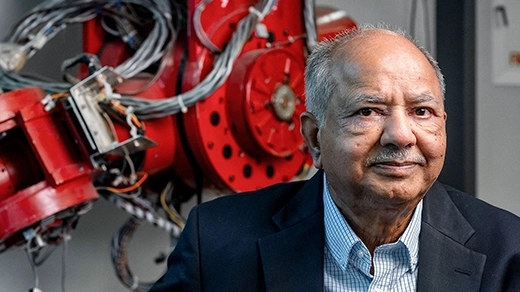 A man in a blue suit sits in front of a red mechanical apparatus