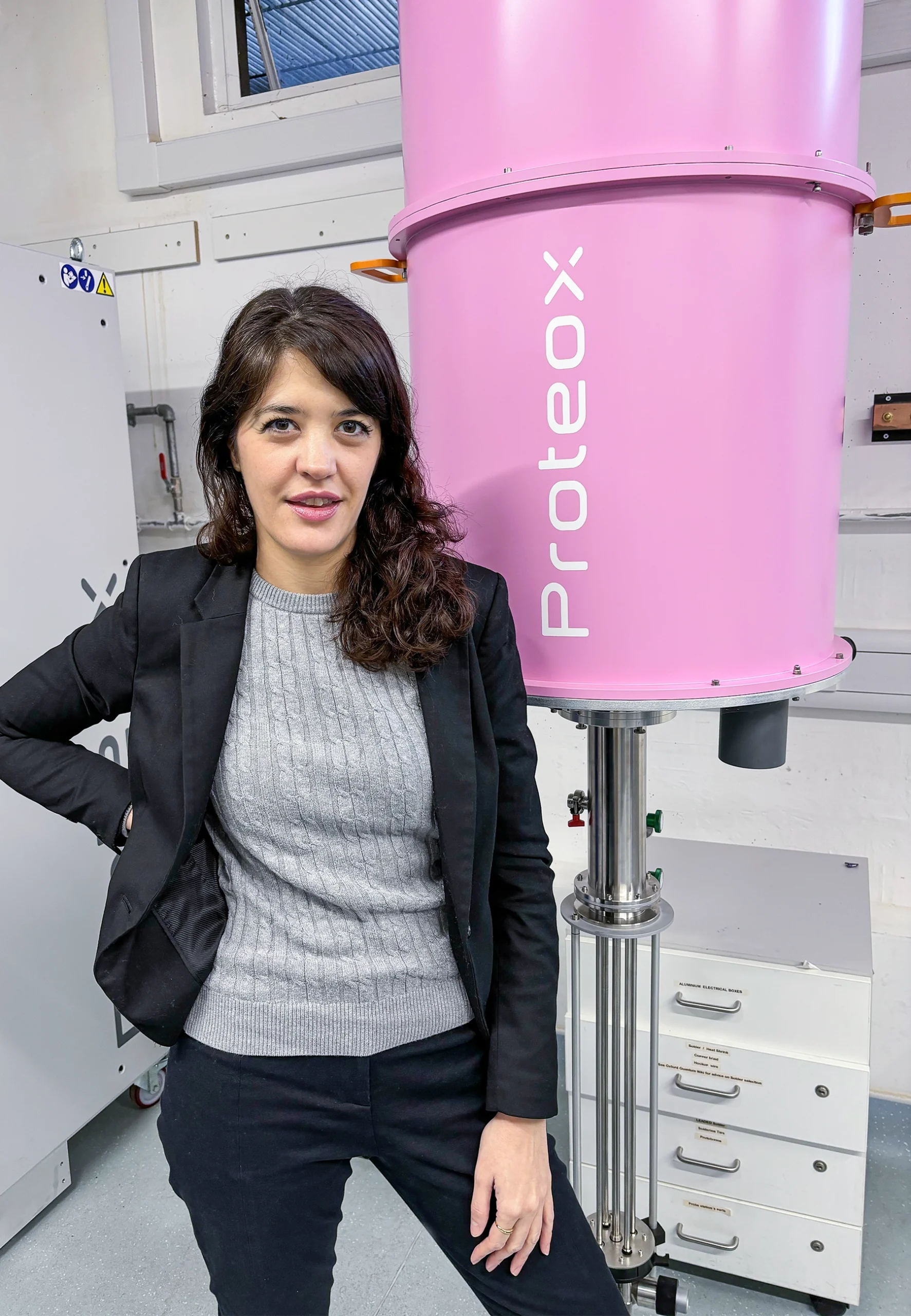 A young woman with brown hair stands next to a hot-pink metal apparatus.