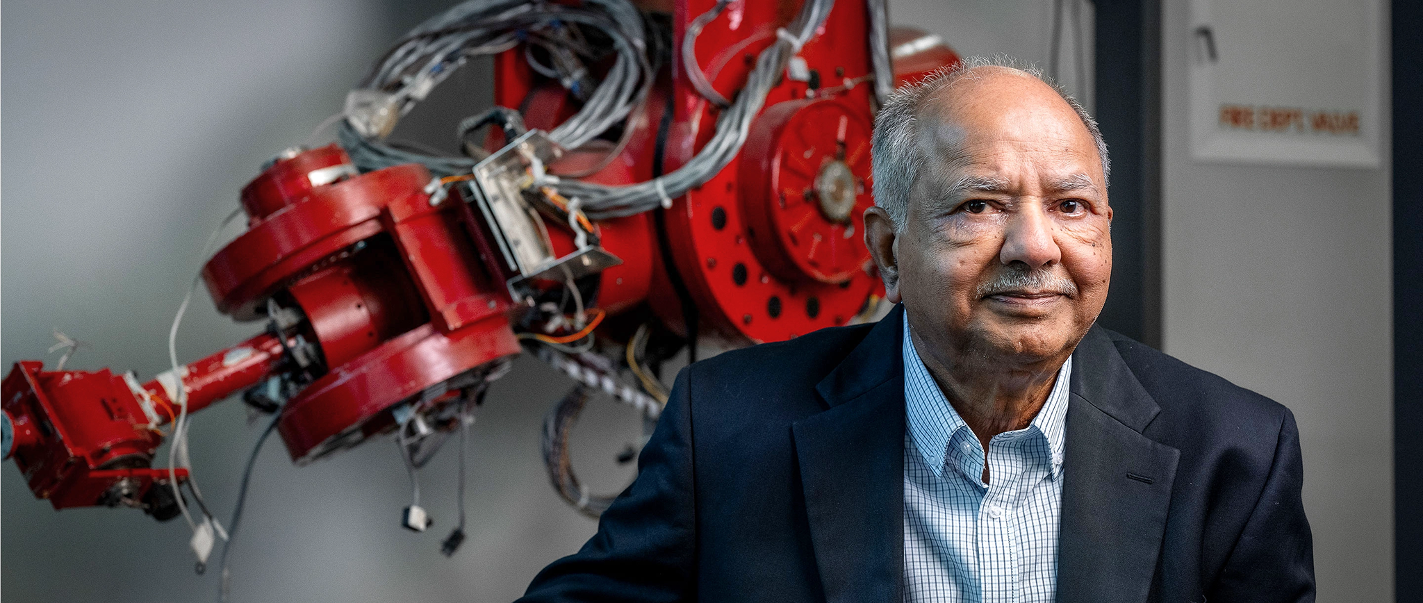 A man in a suit sits in front of a red mechanical apparatus