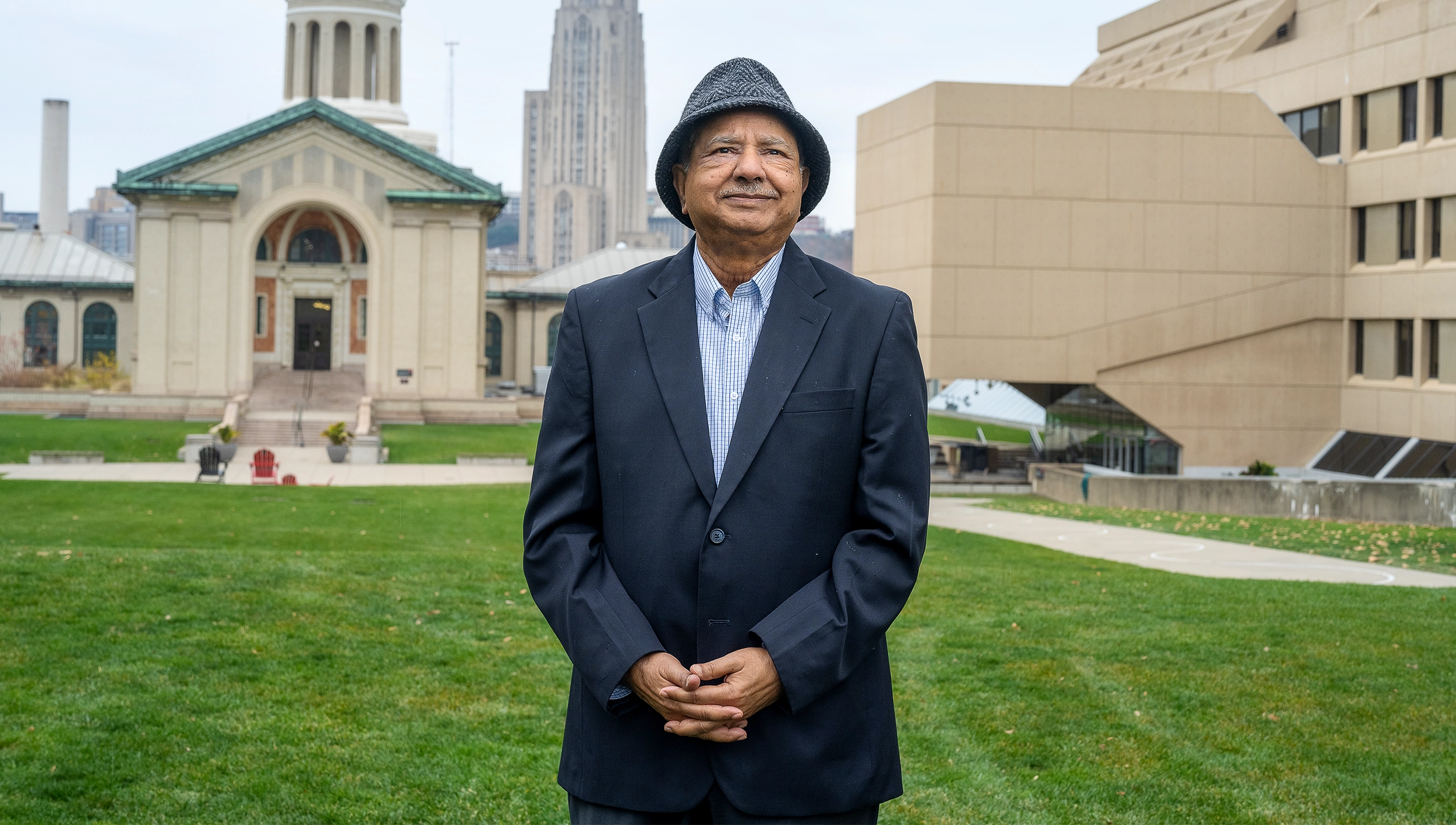 Raj Reddy in a dark suit coat and gray hat stands outside with buildings in the background.