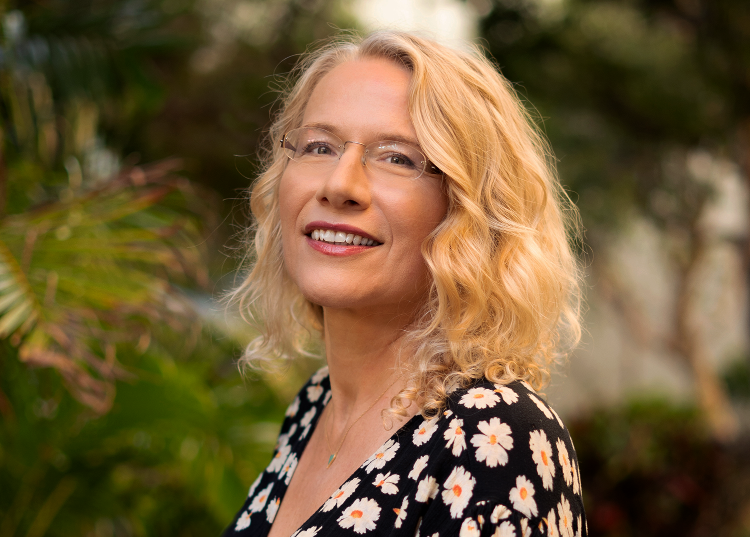 Portrait of a smiling woman with blond hair in a flowery dress.