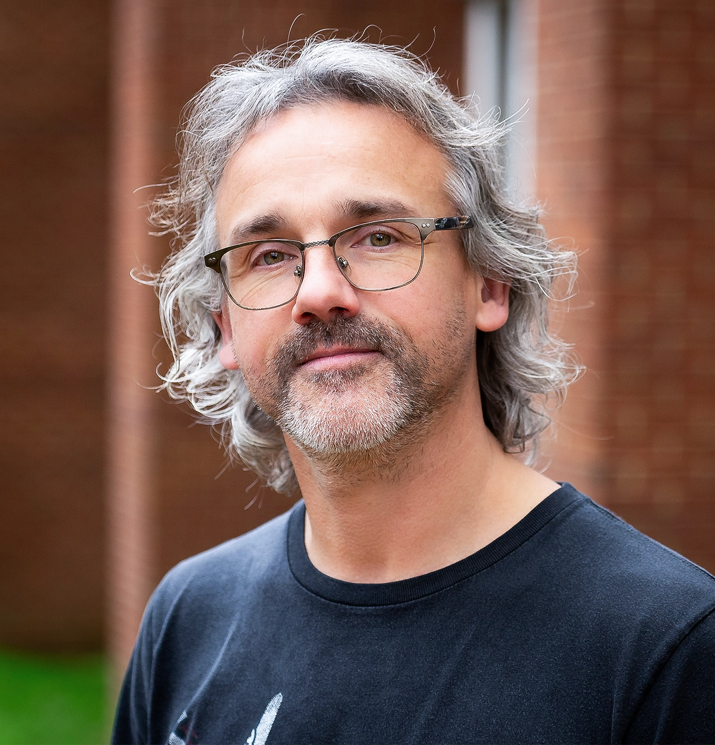 Jeff Mitchell in a black T-shirt in front of a brick building