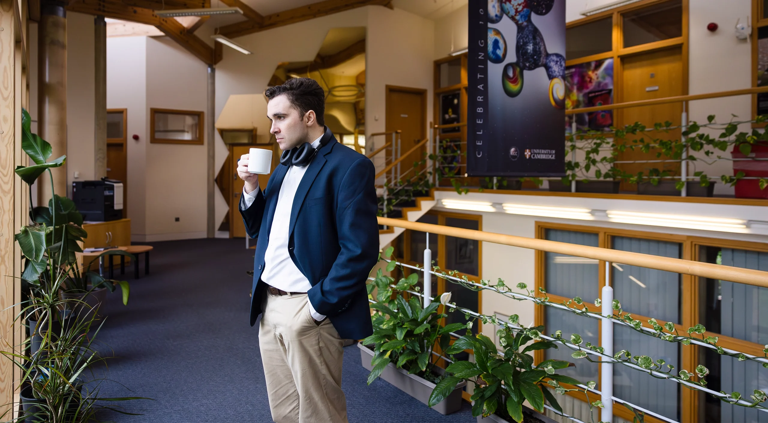 Miles Cranmer in a blue blazer stands in a hallway near some plants and a railing