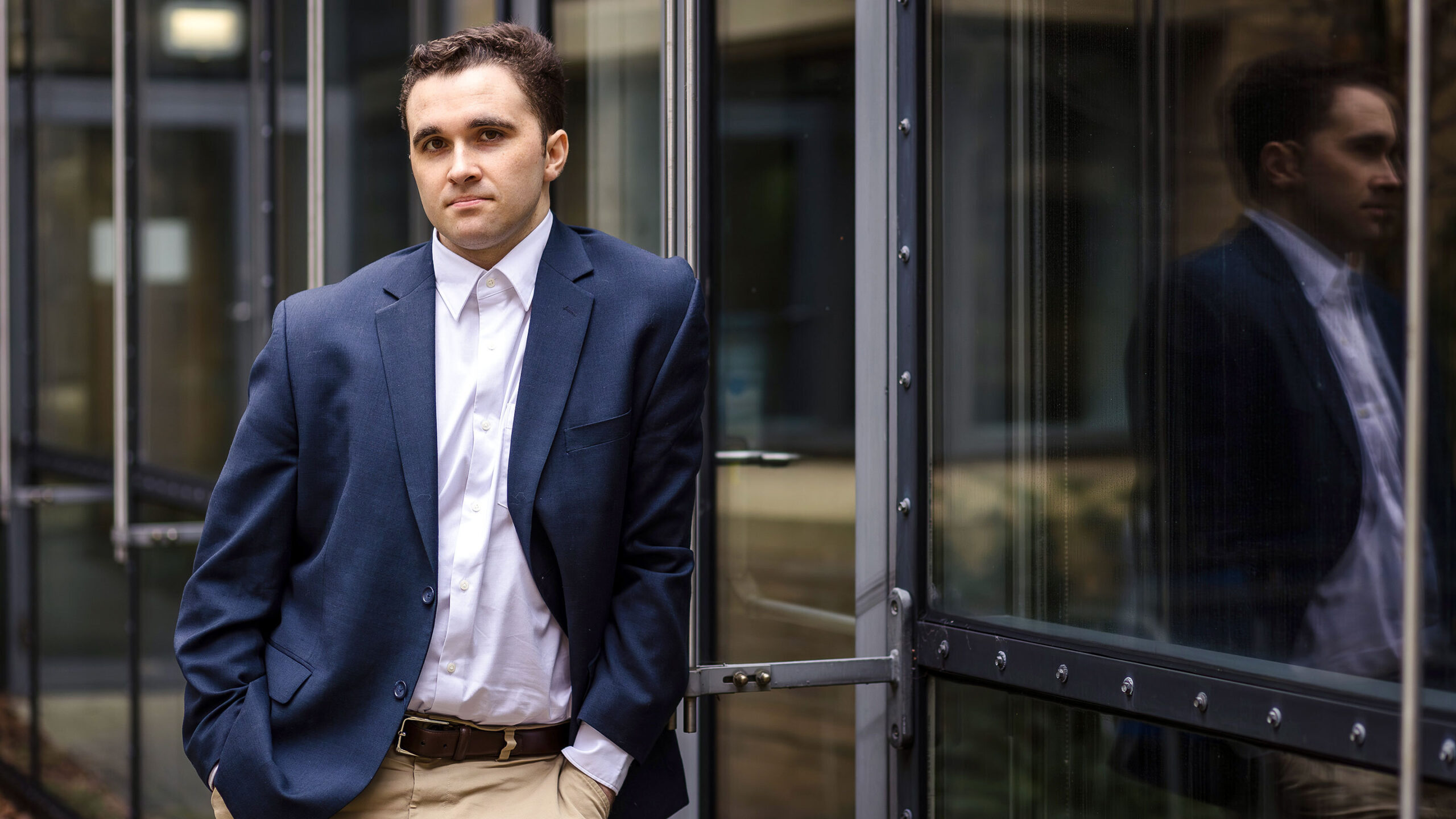 Miles Cranmer in a blue blazer and buttoned up shirt outside a glass building