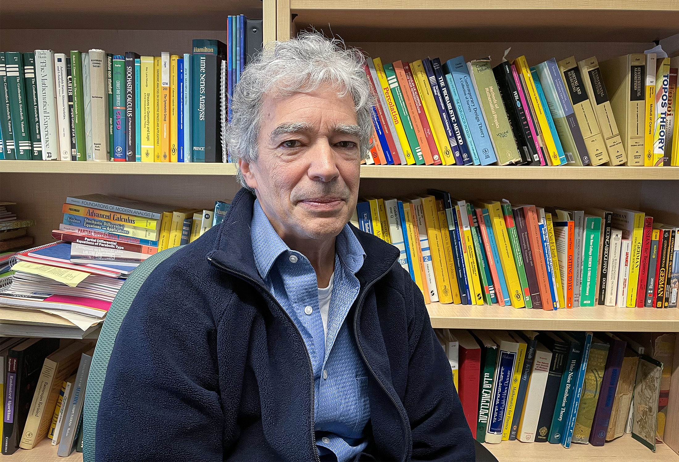 Gray-haired man in front of a bookcase.