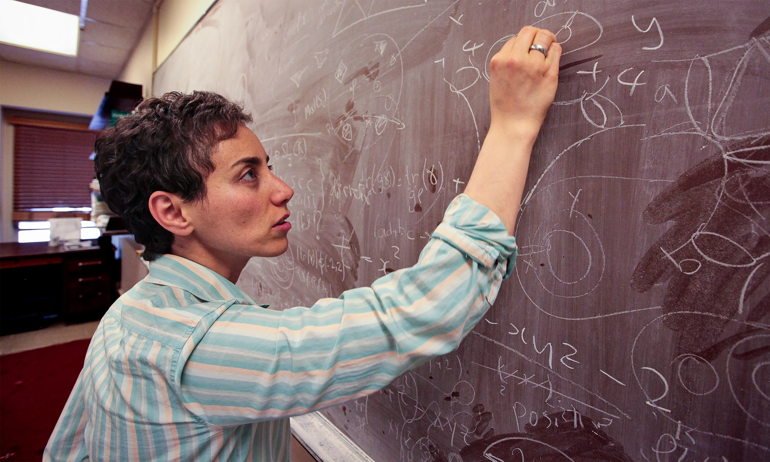 Short-haired woman writing on a blackboard.