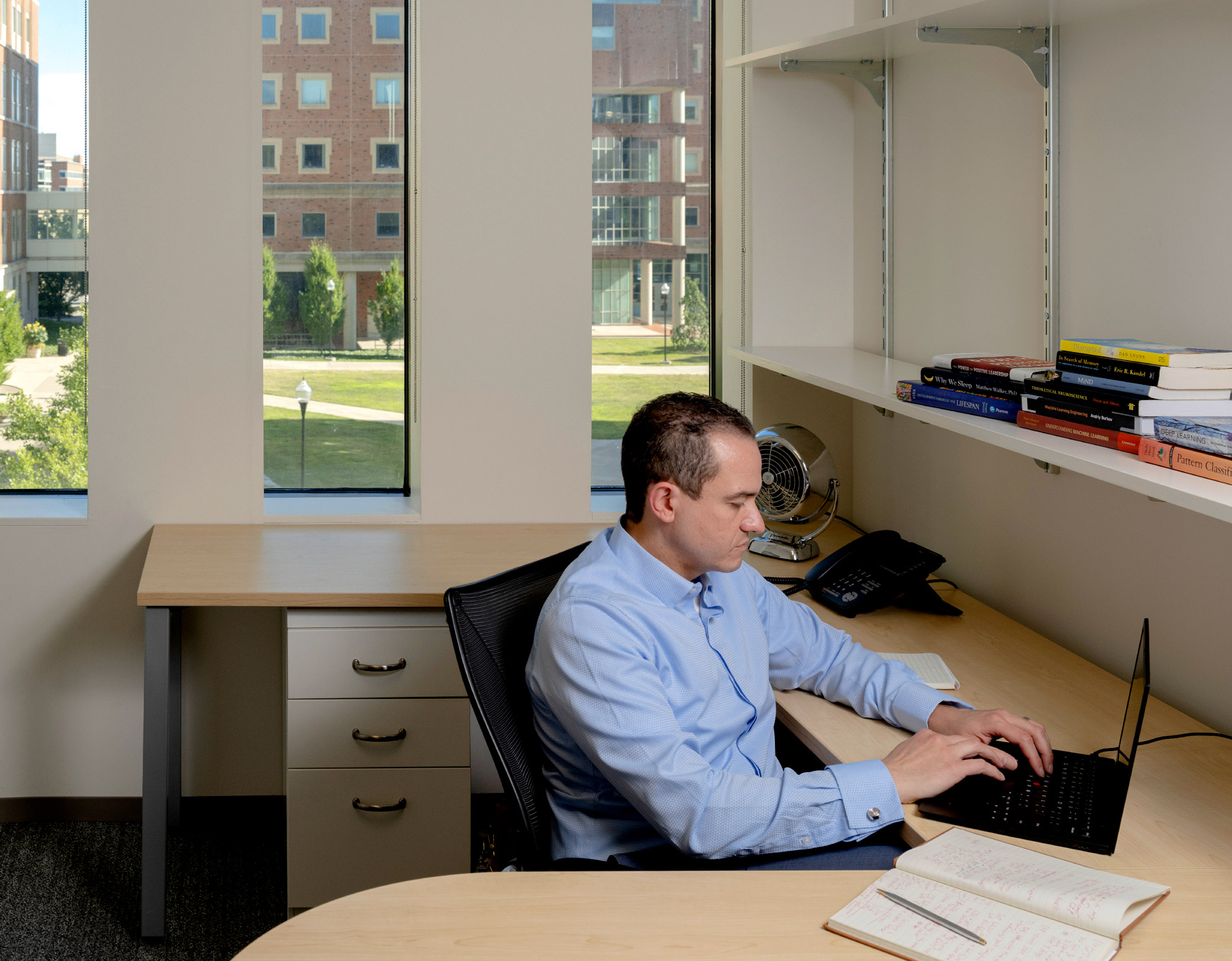 A man in a blue shirt working on a laptop.