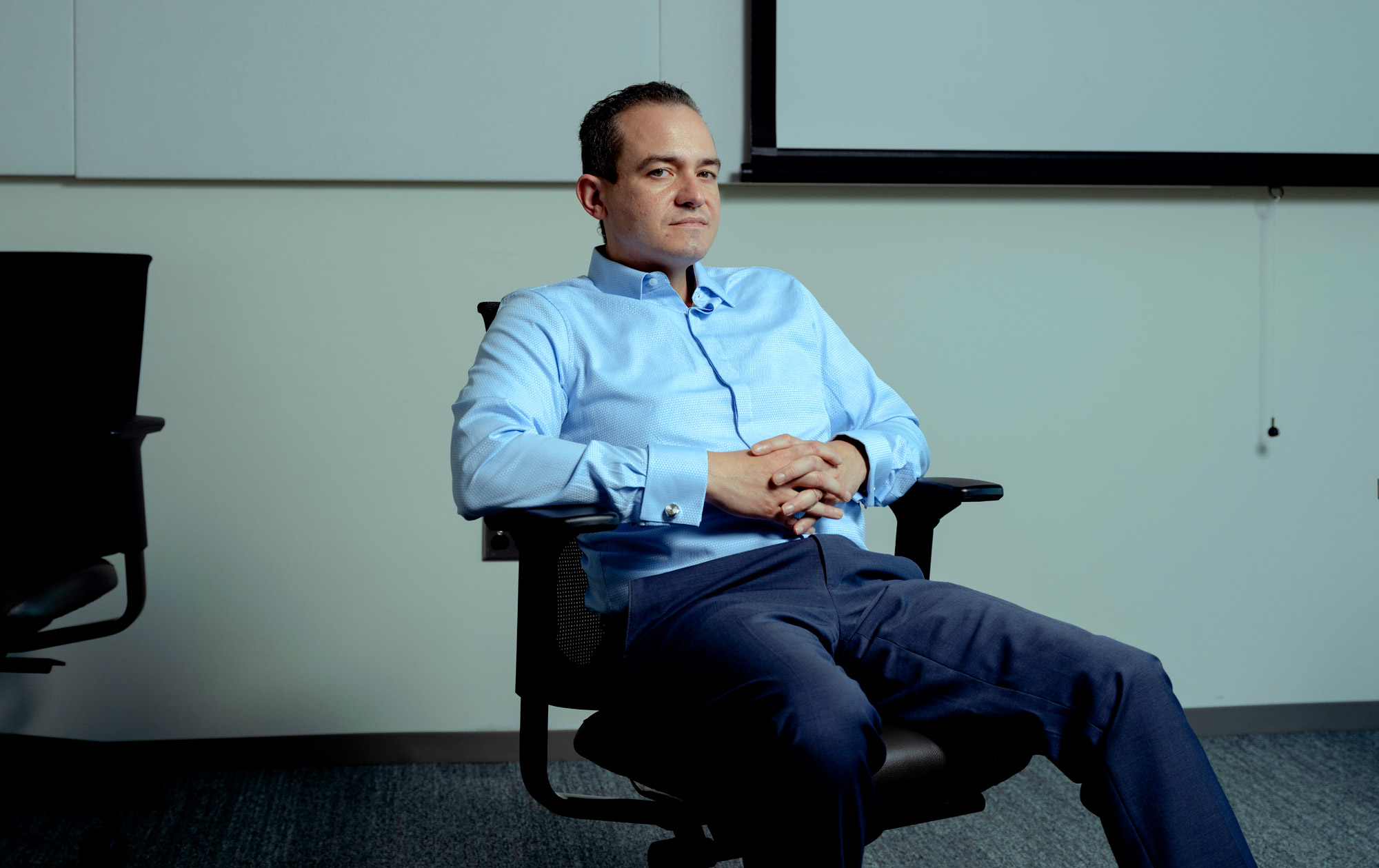 A man in a blue shirt sitting in an office chair.